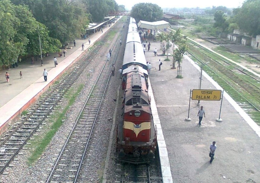 Palam Vihar_a train traveling down train tracks next to a forest